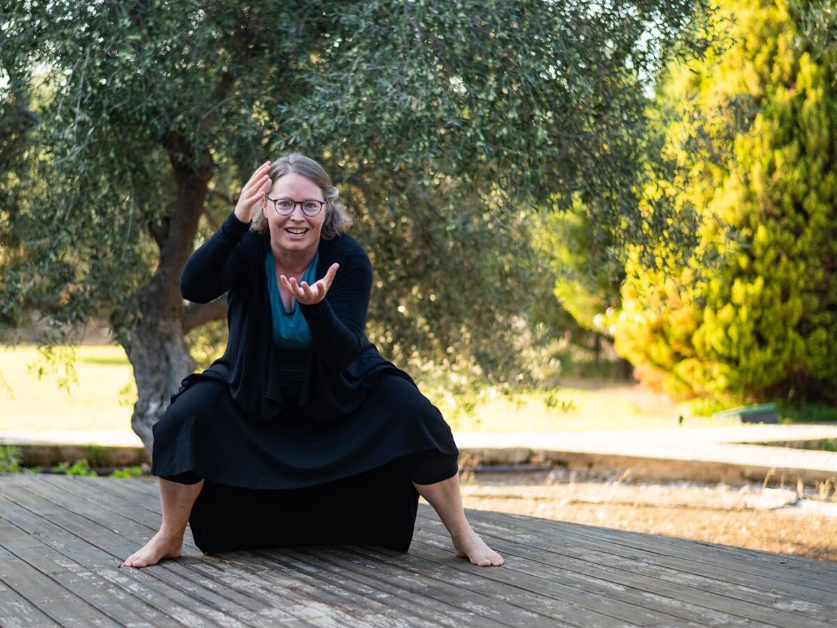 Woman barefoot on wooden platform, crouched and gesturing expressively