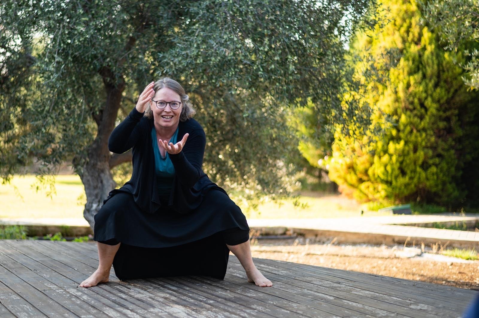 Woman barefoot on wooden platform, crouched and gesturing expressively