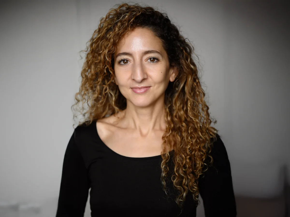 Headshot of Iman Kerroua, associate teaching artist for Physical Lab, wearing a long-sleeve black shirt