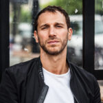 Headshot of Yorgos Karamalegos, Physical Lab founder, wearing a white t-shirt and black leather jacket