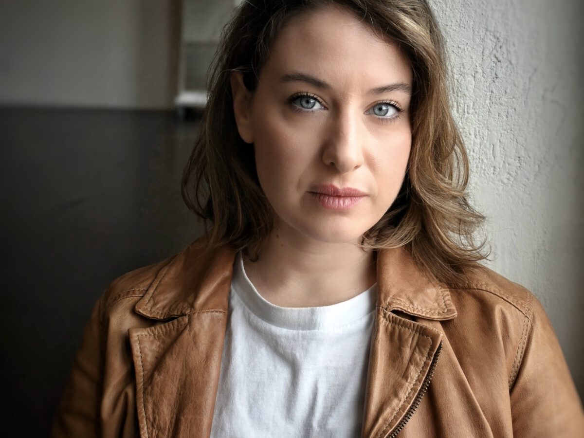Headshot of Jil Clesse, Physical Lab associate teaching artist, wearing a white t-shirt and brown leather jacket