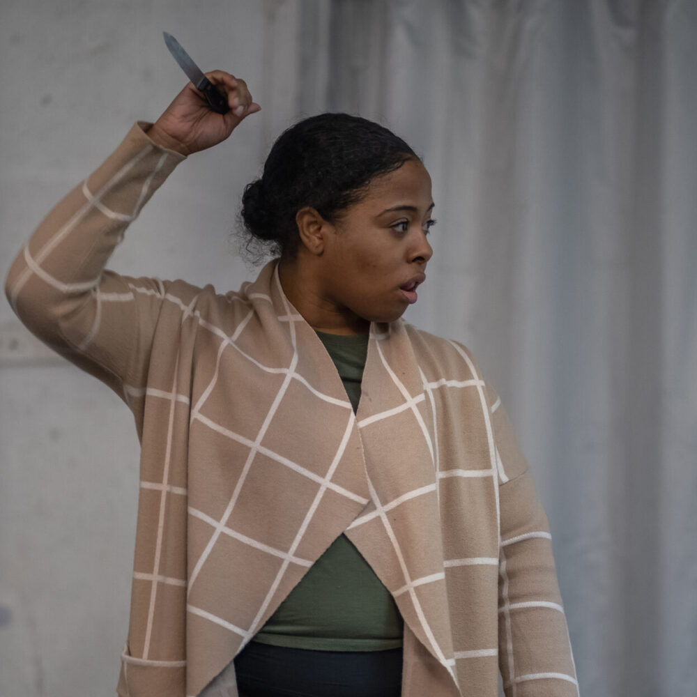 Woman wearing a shawl, right hand extended over her head holding a stage knife