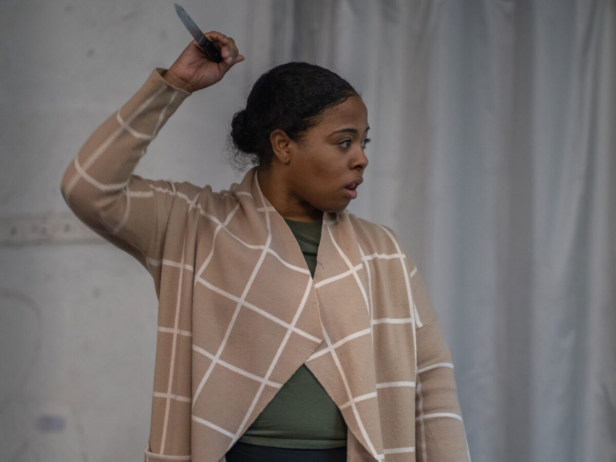 Woman wearing a shawl, right hand extended over her head holding a stage knife
