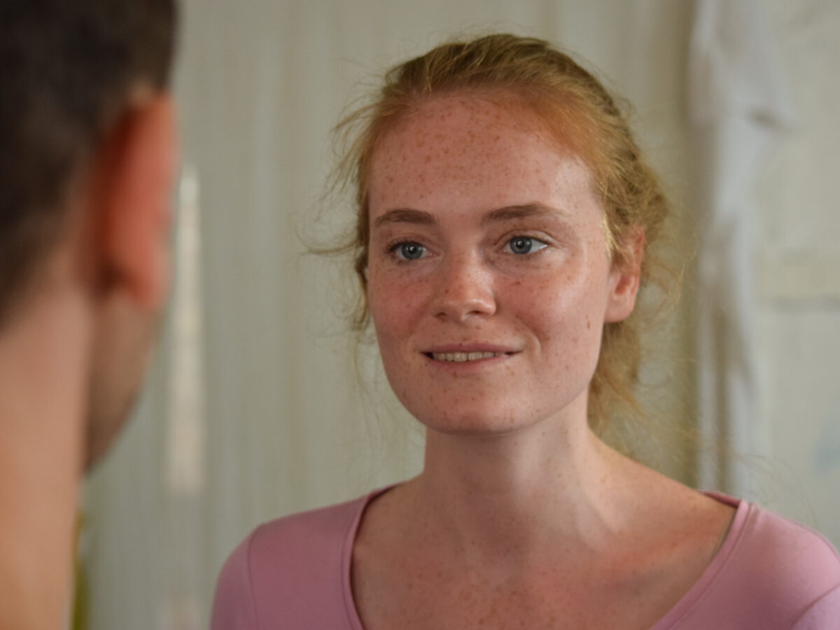 Young woman with freckles smiling at a person in the foreground
