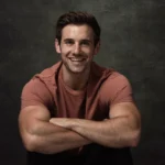 Alex Crockford sitting with arms crossed against dark background and smiling