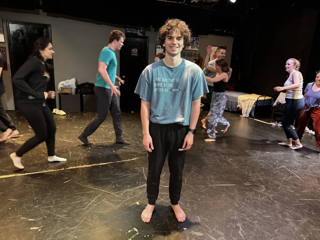 Person in blue t-shirt standing on stage at the Robert Mello Studio